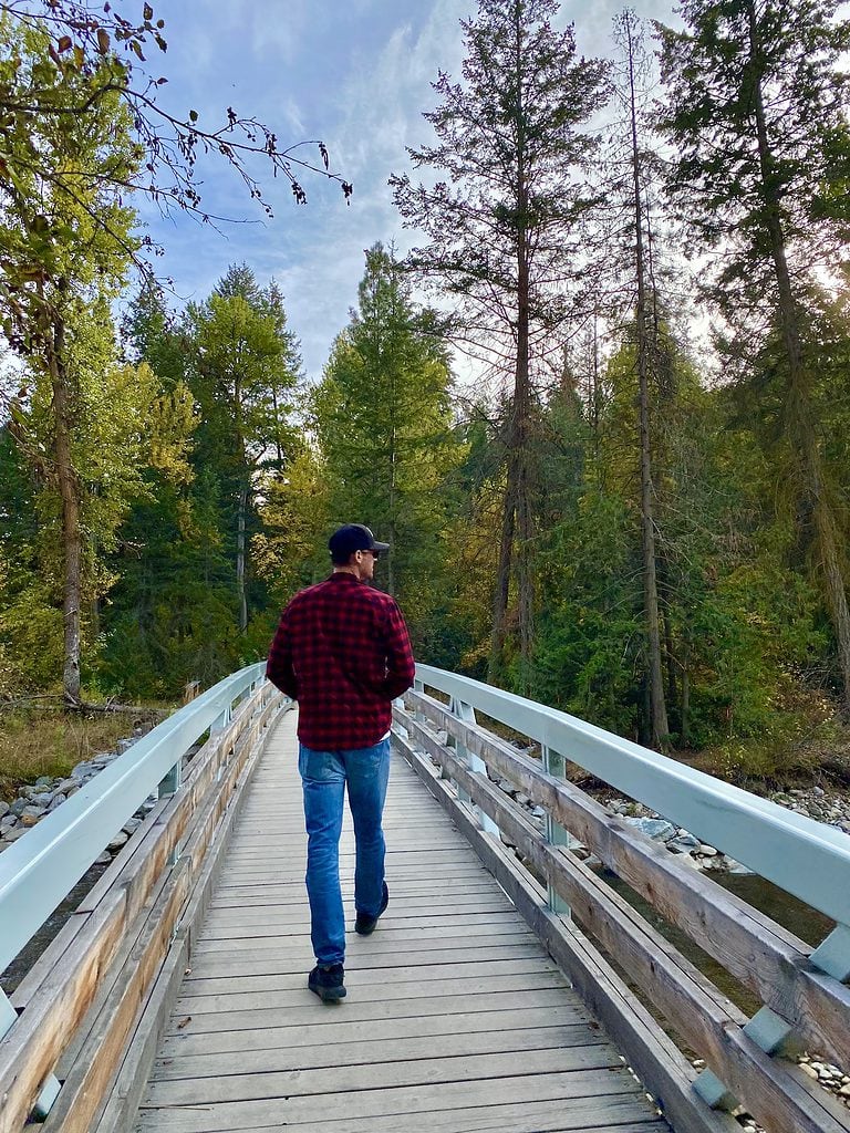 Mikey walking along a bridge over a river in Mission Creek Greenway, Kelowna in the fall