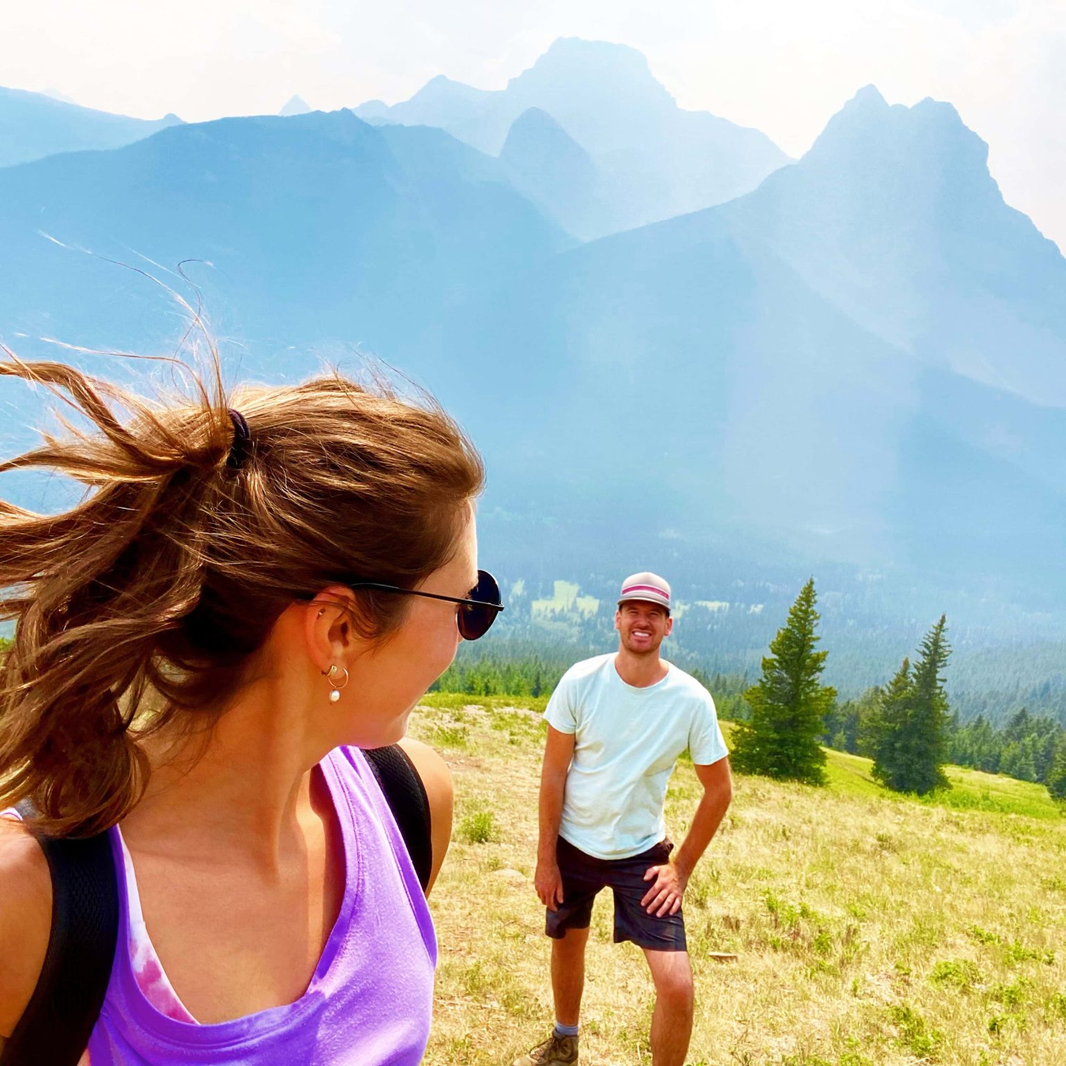 About Us. Mike and Aly hiking in Kananaskis over a green mountainside, Alberta