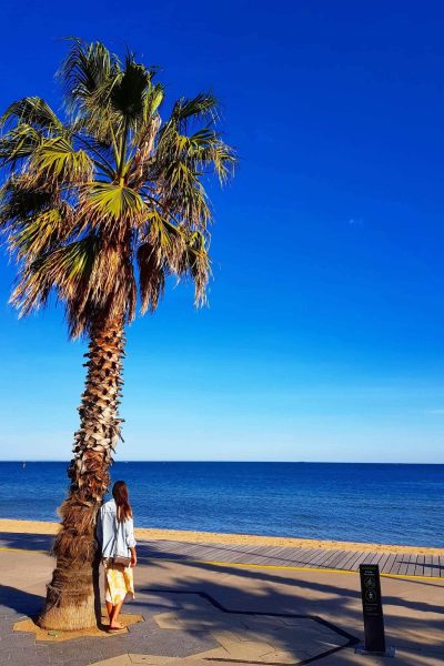 Aly standing next to a palm tree at St. Kilda Beach, Melbourne, Australia